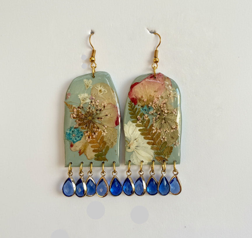 Pair of earrings with floral and blue teardrop designs on a grey background