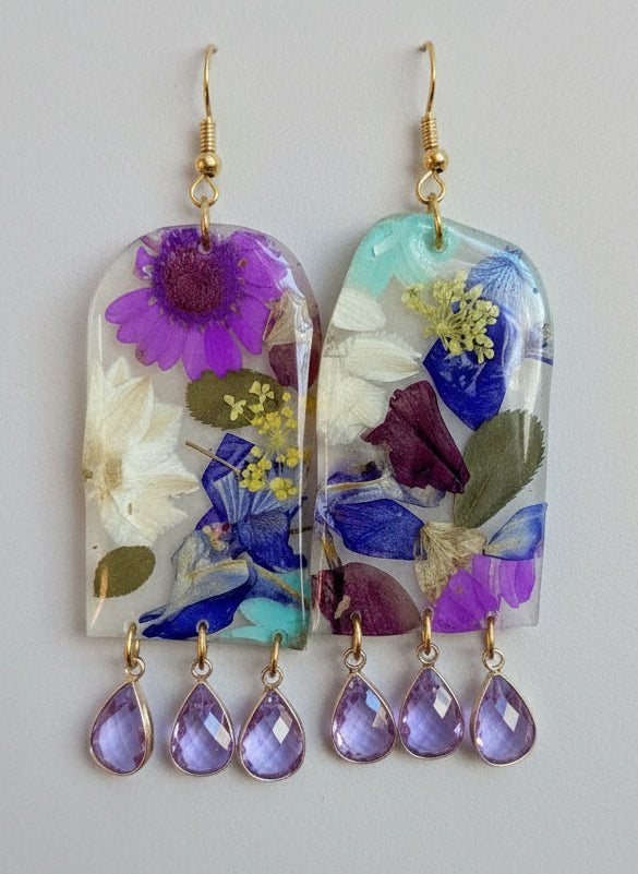 Pair of earrings with floral and teardrop designs on a light blue background