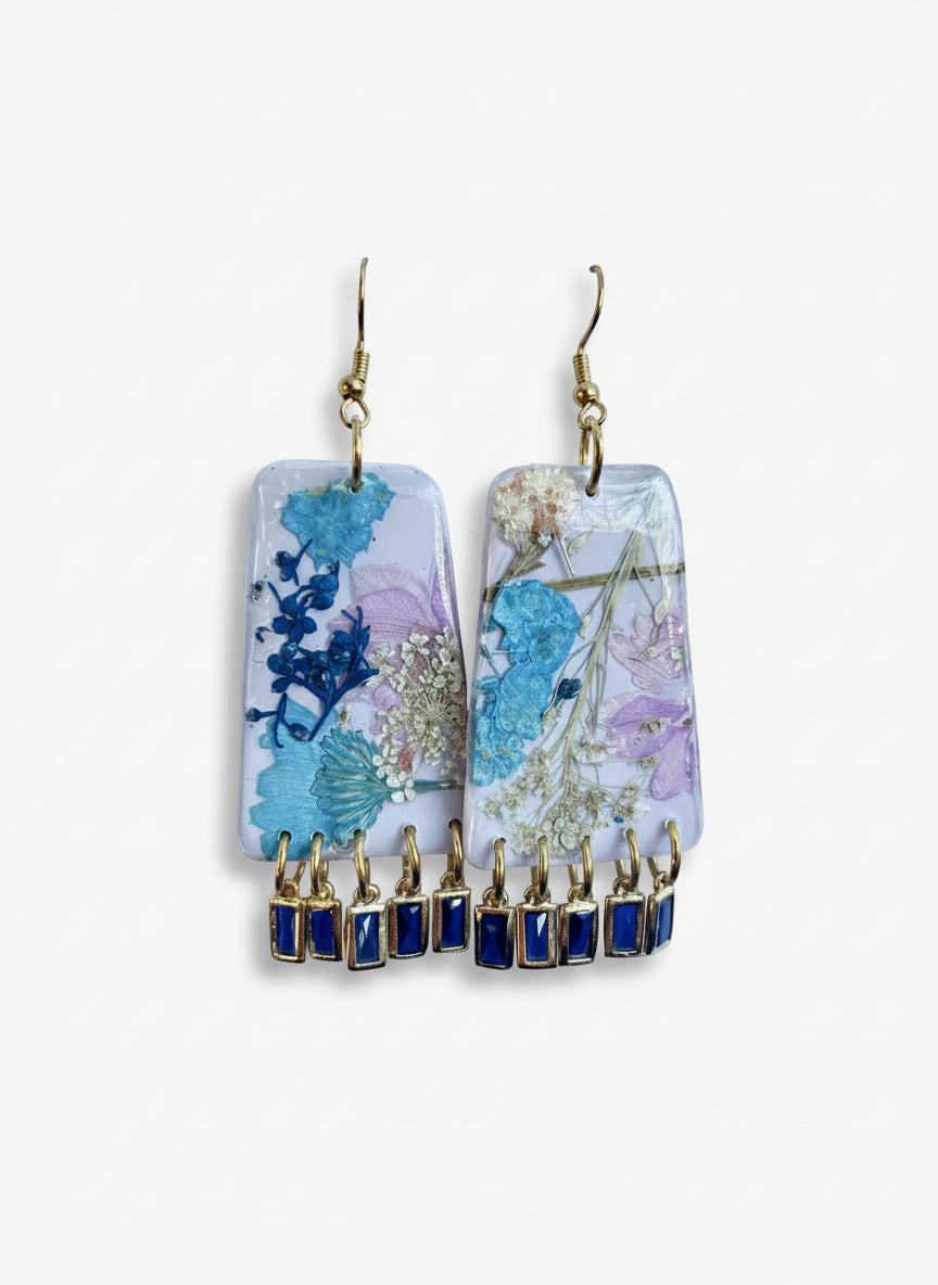 Pair of earrings with floral design and blue gemstone drops on a light blue background