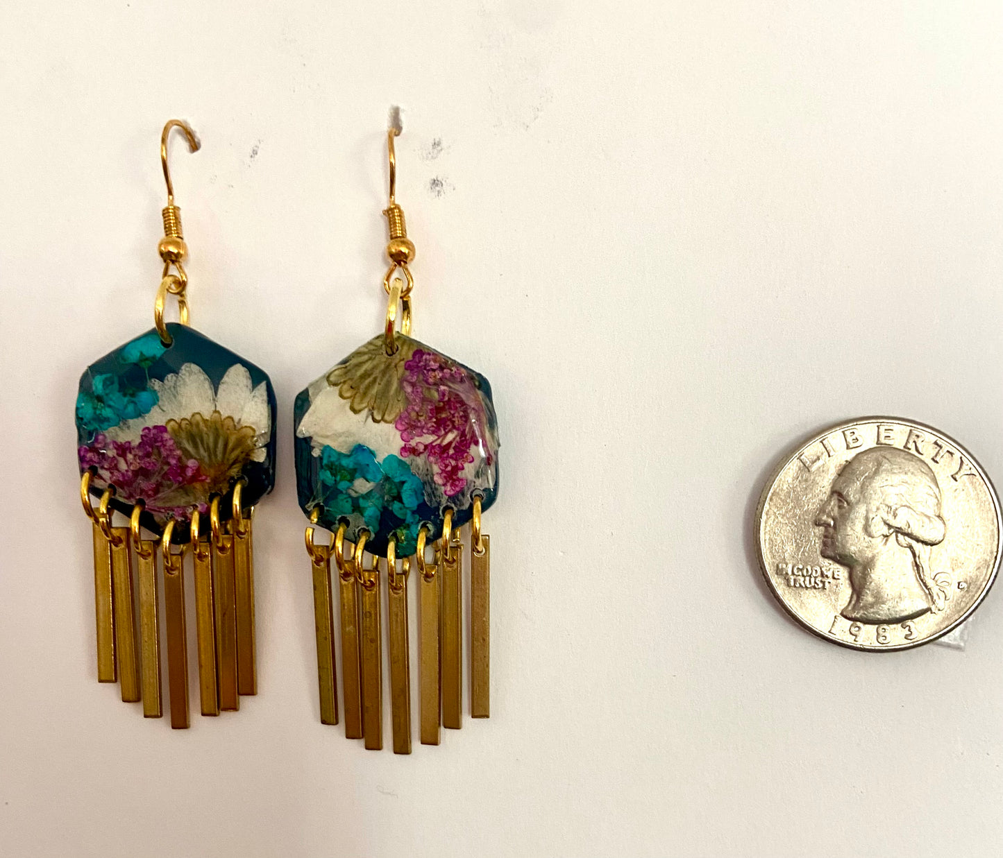 Floral earrings with gold fringe next to a quarter for scale on a white background